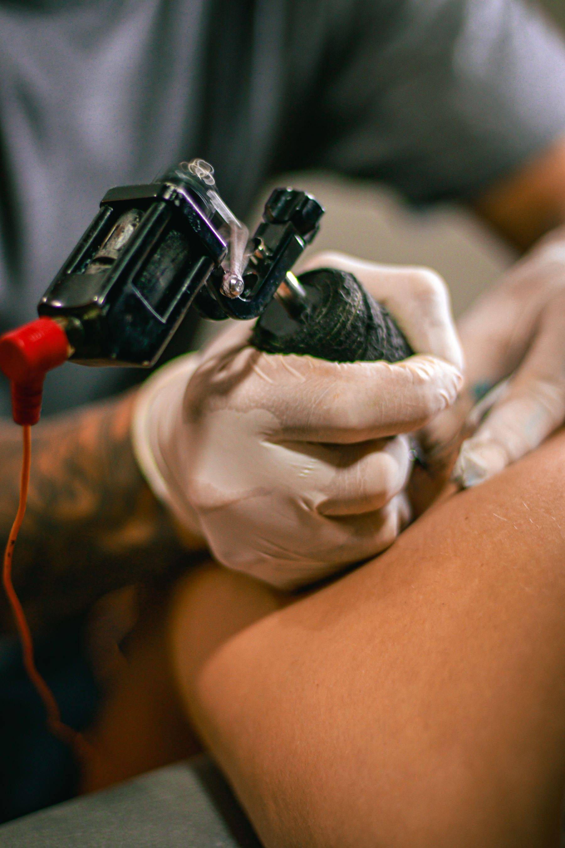 Une main gantée tient une machine à tatouer au-dessus d’un bras.