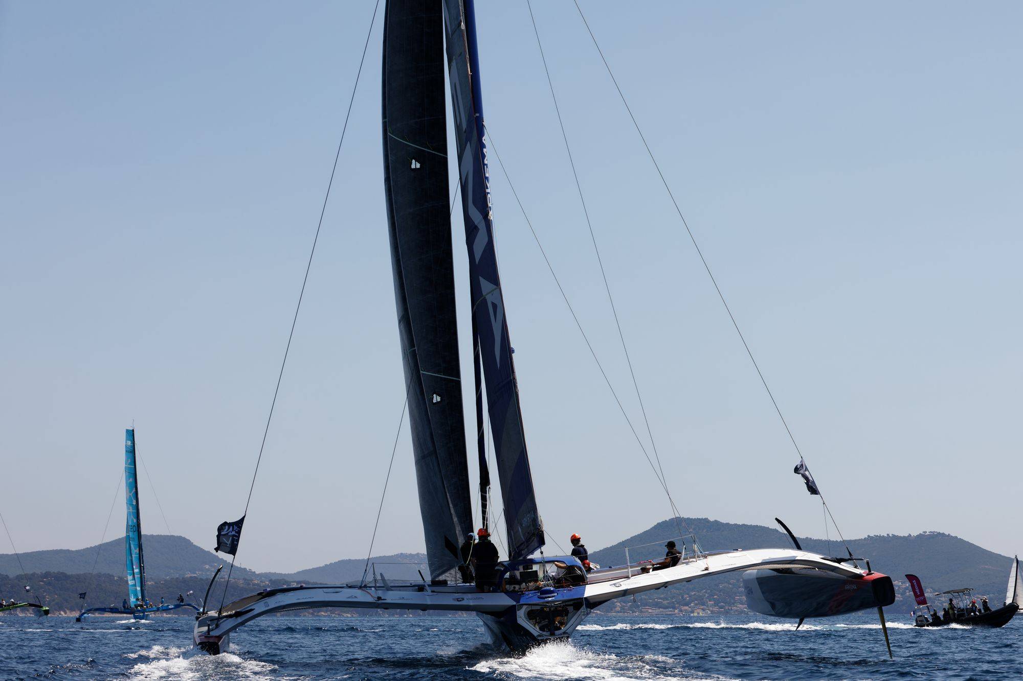 Un trimaran de course au large file sur la mer, un flotteur soulevé au-dessus de l’eau.